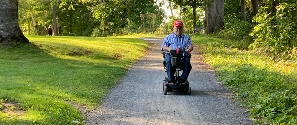Un adulte sur un scooter a mobilité sur une de surface large de gravier compacté