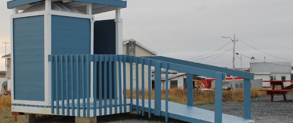 Une toilette extérieure bleue et blanche qui offre une rampe d’accès pour fauteuil roulant aux usagers. 