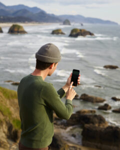 Façons de passer au vert : un adulte portant un haut vert lors d'une randonnée prenant une photo de l'océan et des rochers