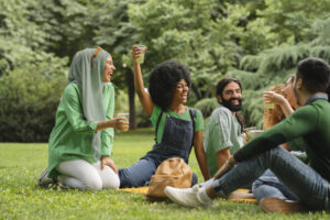 Un groupe d'adultes portant du vert et tenant des tasses transparentes avec un liquide vert assis sur l'herbe participant à des façons de passer au vert pour la Saint-Patrick