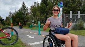 Woman using a wheelchair gives a thumbs up on an accessible trail
