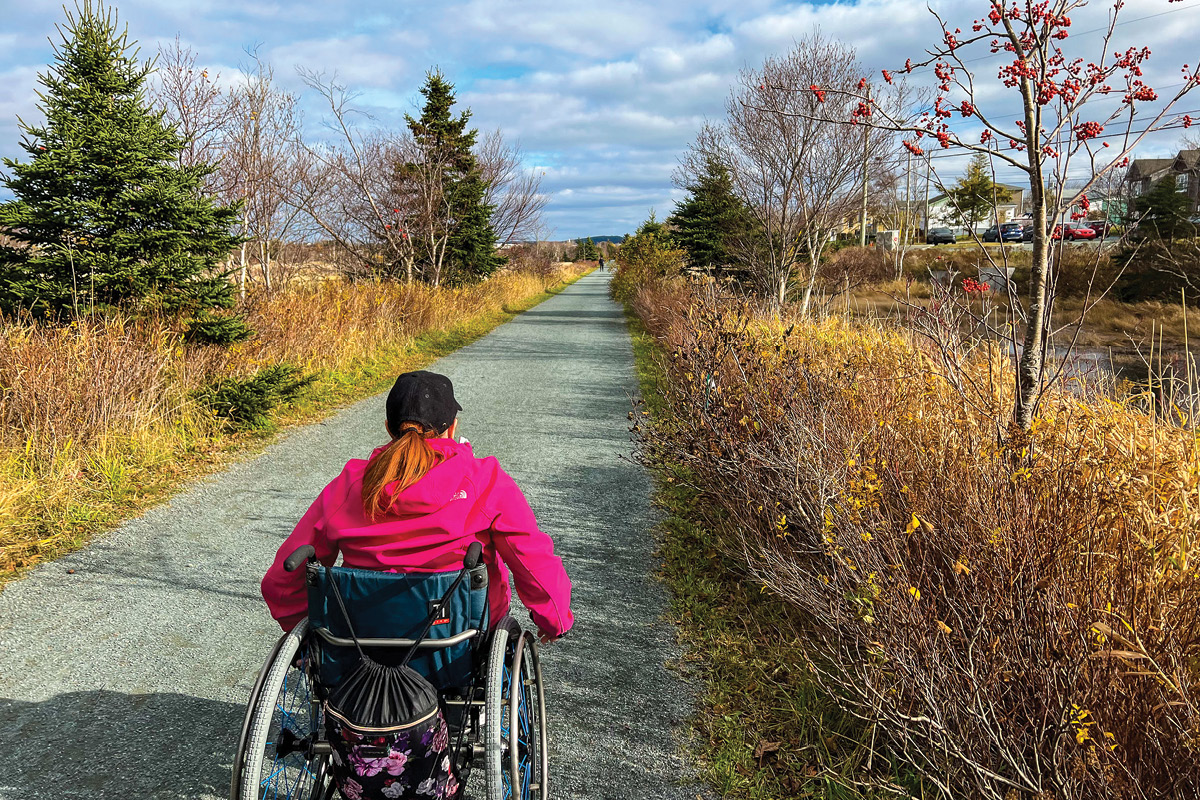 An adult in a wheelchair on a gravel surface trail 