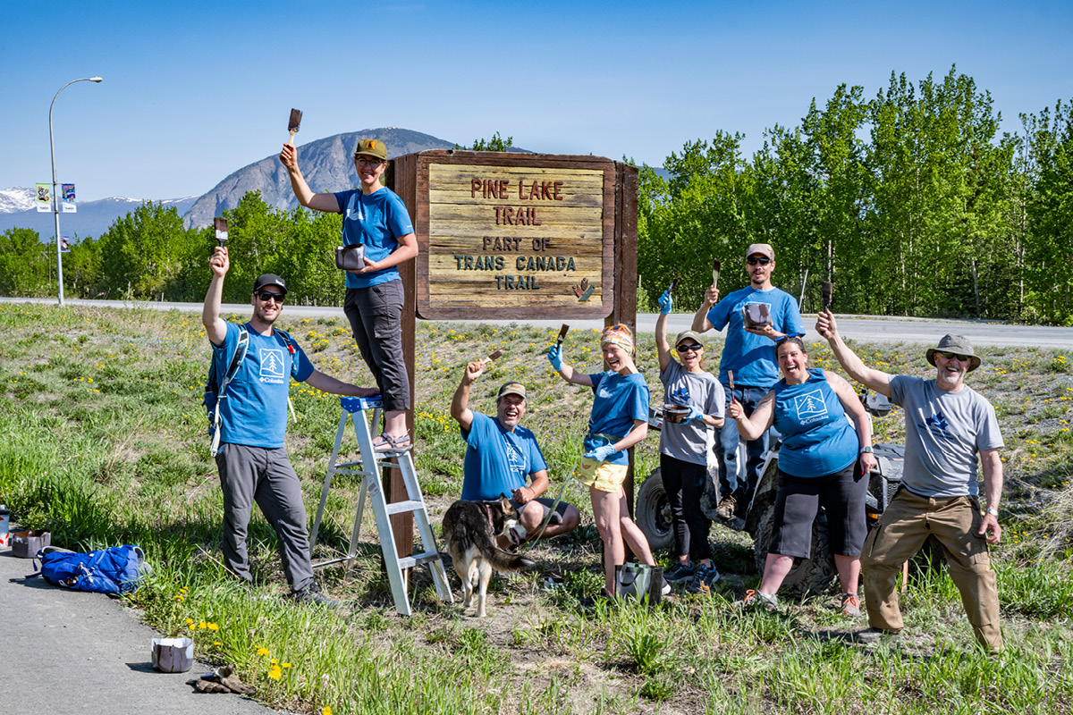 Trail group holding up paint brushes in front of the Pine Lake Trans Canada Trail sign