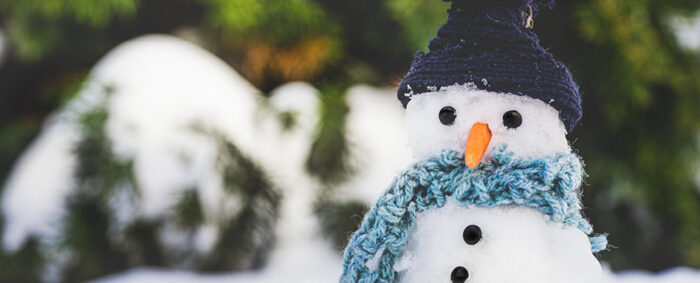 Close up of a snowman with button eyes, a carrot nose, wearing a winter hat and scarf.