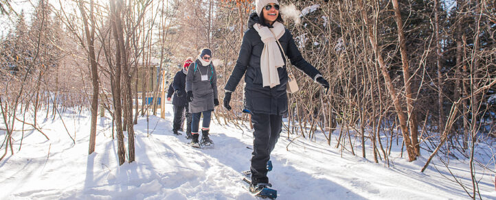 A group of adults walking on snow shoes down a snowy path