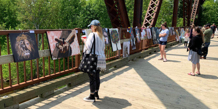 Art being displayed on a bridge rail with onlookers walking by