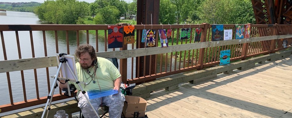 An artist working on art on the Bill Thorpe Walking Bridge with community art displayed behind them.
