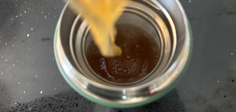 Warm ginger apple cider being poured into a thermos