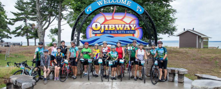 Cyclists of the Great Waterfront Trail Adventure standing in front of the welcome sign for Ojibway Park sign 
