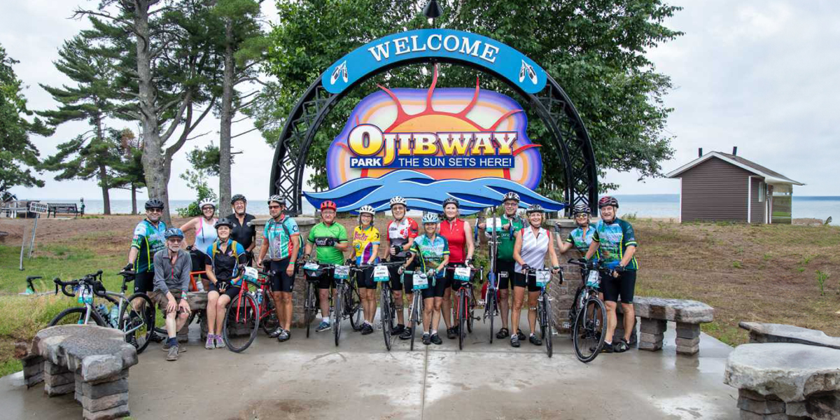 Cyclists of the Great Waterfront Trail Adventure standing in front of the welcome sign for Ojibway Park | Cyclistes de la Grande aventure sur le sentier riverain devant le panneau de bienvenue du parc Ojibway