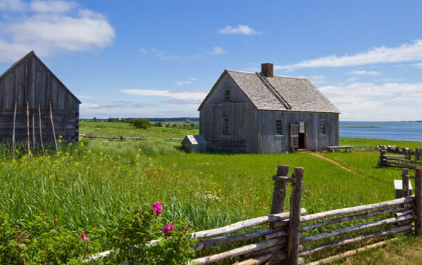 Two old wooden houses on a grassy field near the water in North Rustico. | Deux vieilles maisons en bois sur un terrain herbeux près de l'eau à North Rustico.