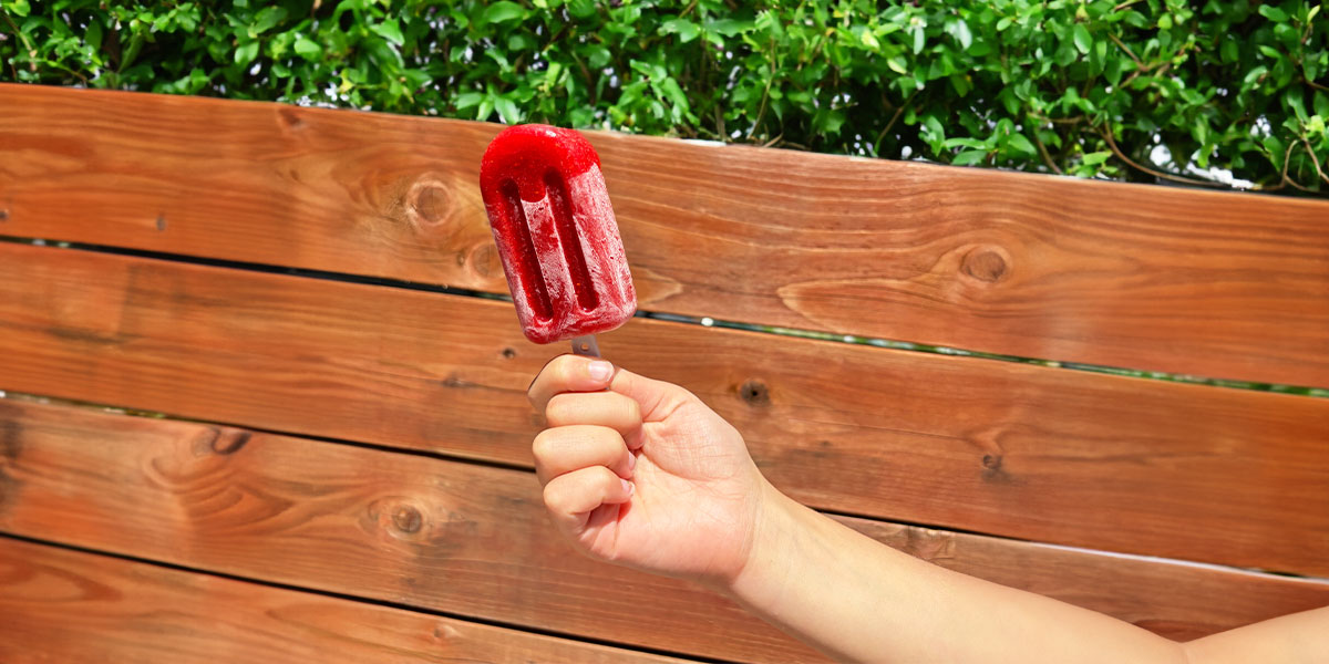 Person holding red popsicle in front of wooden bench. |  