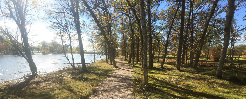 The Pinawa Trail features a winding path that guides visitors to a river framed by vibrant trees. Le sentier Pinawa présente un chemin sinueux qui guide les visiteurs vers une rivière encadrée d'arbres vibrants.