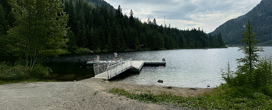 A scenic dock at Cottonwood Lake Regional Park, with calm waters and towering mountains creating a beautiful backdrop. Un quai pittoresque au parc régional de Cottonwood Lake, avec des eaux calmes et des montagnes imposantes créant une magnifique toile de fond.