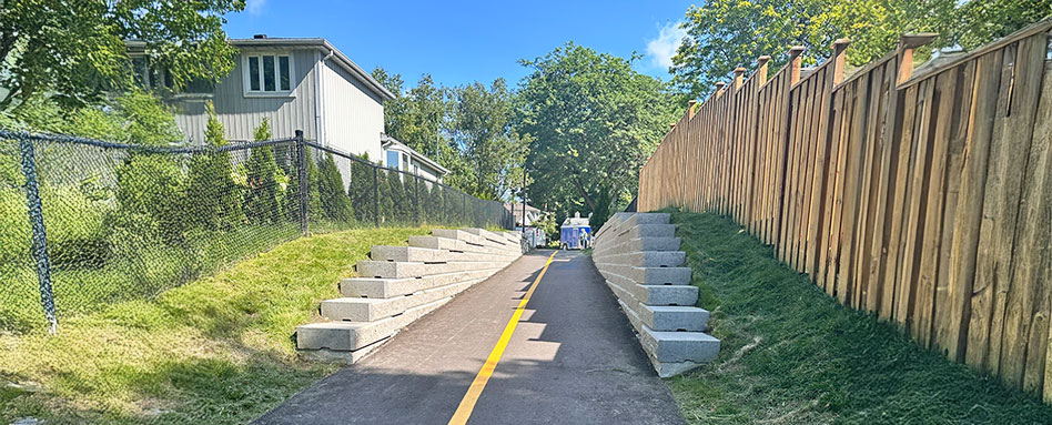 A bike path bordered by concrete blocks at Bruce Handscomb Memorial Park in Pickering, showcasing a serene outdoor setting. Une piste cyclable bordée de blocs de béton au parc commémoratif Bruce Handscomb à Pickering, mettant en valeur un cadre extérieur serein.