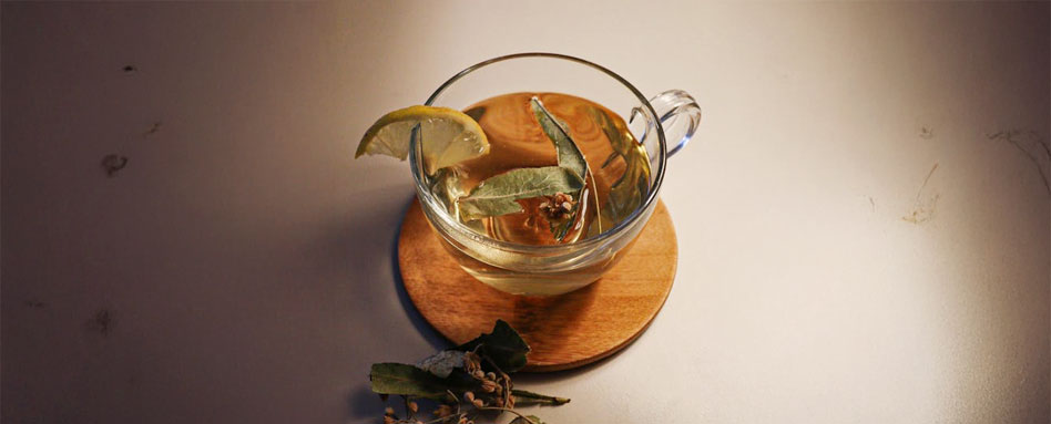 A glass cup filled with green tea, garnished with fresh lemon slices, resting on a wooden surface. Une tasse en verre remplie de thé vert, décorée de tranches de citron frais, posée sur une surface en bois.