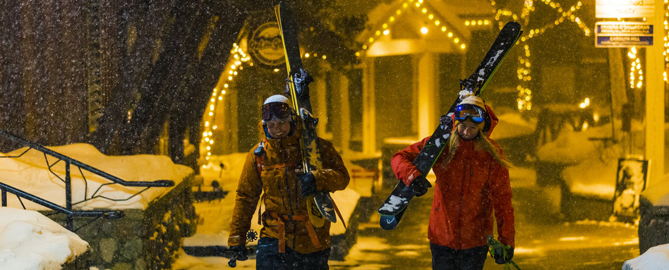 two women smiling holding ski gear on a snowy night