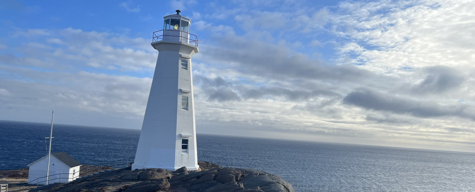 white lighthouse at Cape Spear, Newfoundland and Labrador—the easternmost point in Canada—overlooking the Atlantic Ocean under a partly cloudy sky.