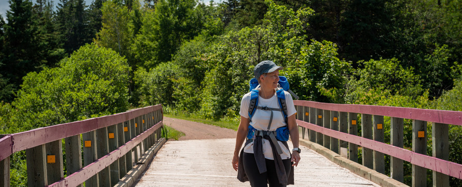 Solo hiker crossing a wooden bridge on the Celtic Shores Coastal Trail in Nova Scotia | Personne en randonnée franchissant un pont de bois sur le Celtic Shores Coastal Trail, en Nouvelle-Écosse.