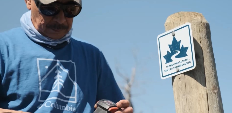 A person adjusts a drill after installing a square Trans Canada Trail sign on a wooden post.
