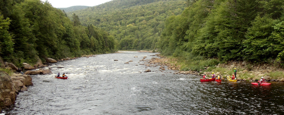 people in canoes on white water rapids with forrested area behind