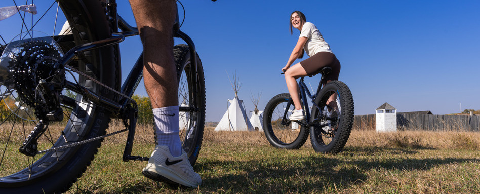 people on bikes in a field with teepees and blue skies behind