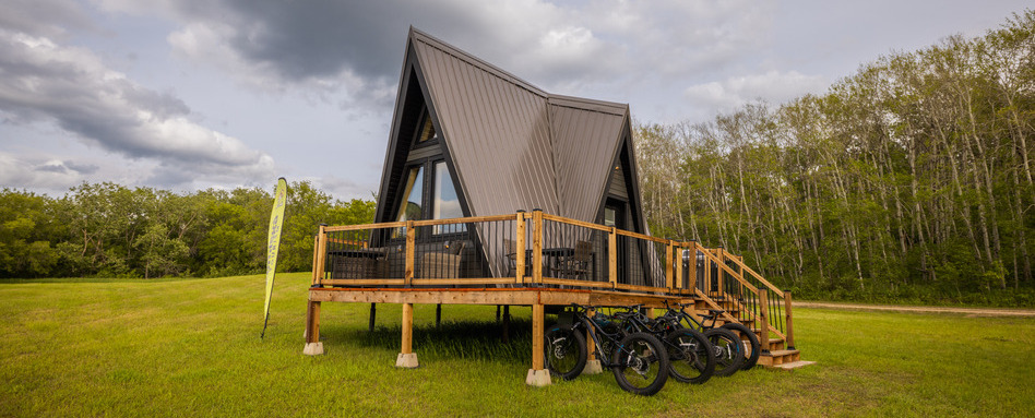 mobile home on a wooden base with bikes attached in a field with cloudy skies 