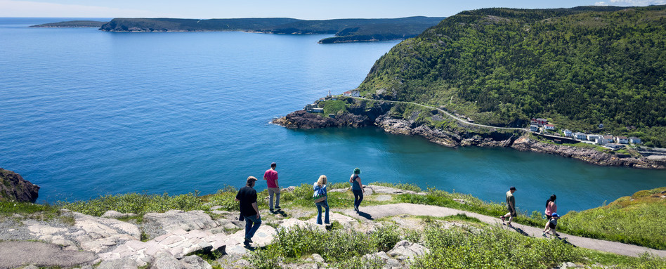 people hiking on a trail overlooking mountains and sea below