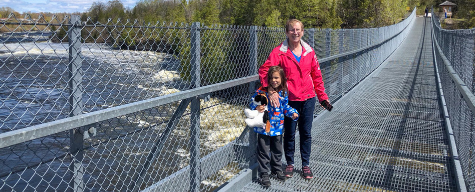 woman and child posing on a bridge with white water and trees behind