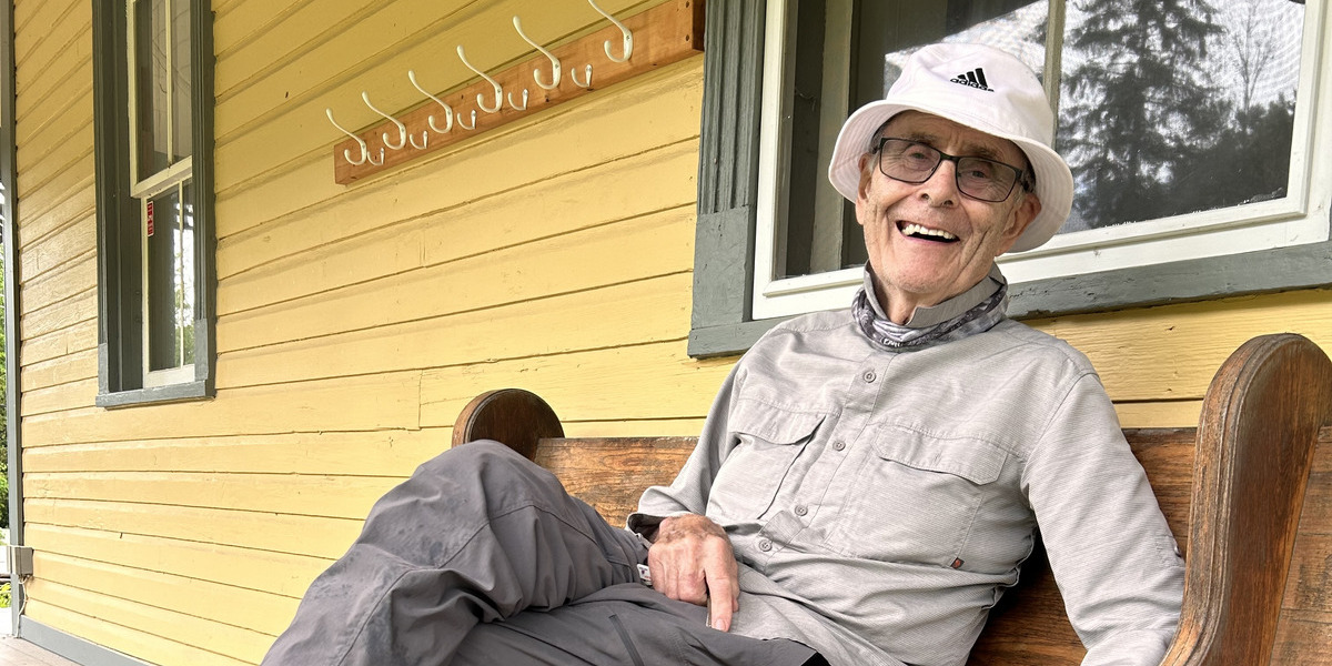 QC_Web story_Feature image_Volunteer recognition Ken Bouchard_credit Sentier Wakefield Trails | Sentier Transcanadien Man sitting on bench outside a yellow house, smiling at the camera.