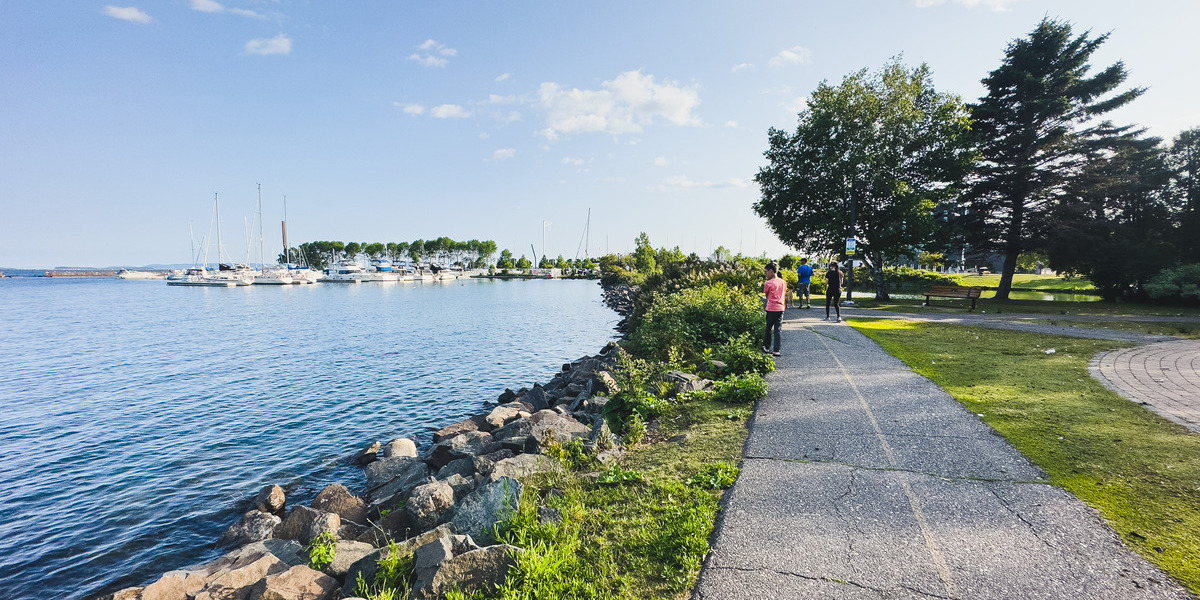 people walking on bike trail on sunny day with water alongside
