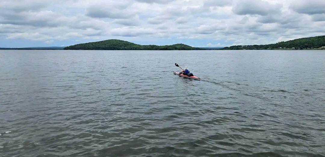 Aidan kayaks in open water with coastline in the background.