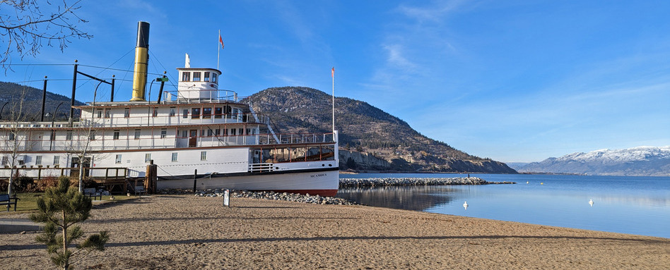 large boat parked in waterfront area with mountains behind on a sunny day