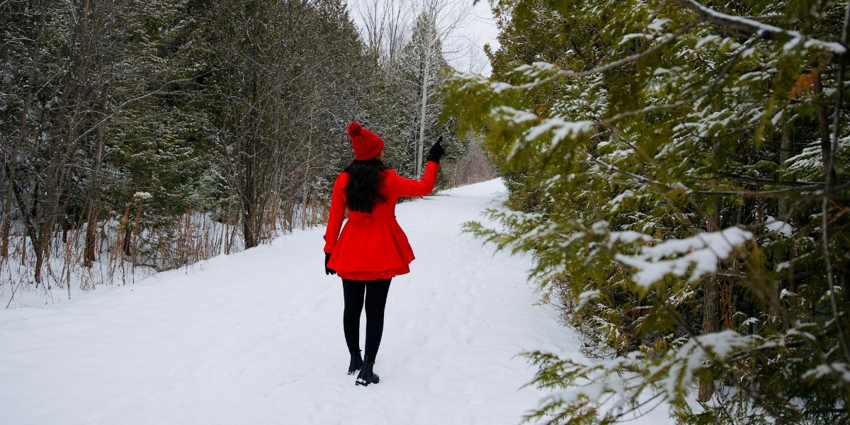 00Feature image_ON_Caledon Trailway_credit Travels with Asavari | Sentier Transcanadien woman in red dress walking on a snow covered trail in forest