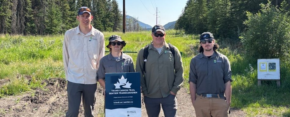people holding a trail sign smiling on sunny day