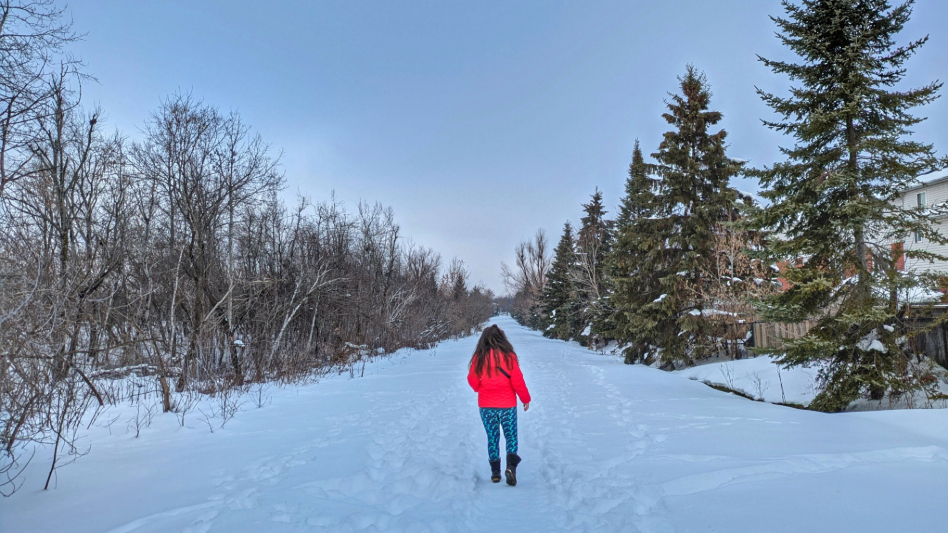 woman walking on snow covered trail into a forest
