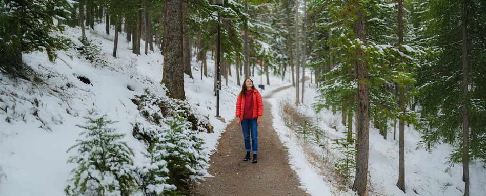 woman in a forest in winter smiling above at snow covered trees
