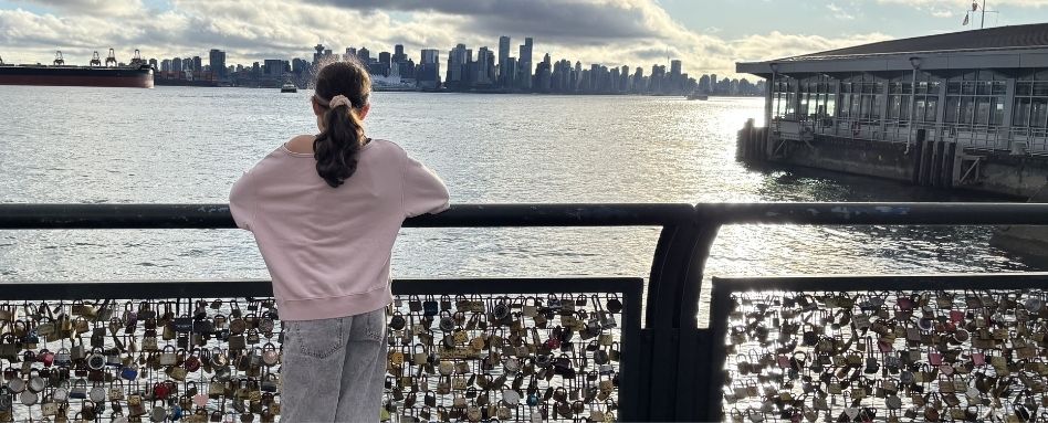 girl standing on lock bridge overlooking skyline and water