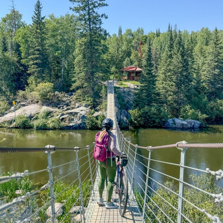 woman on a bridge over water area with bike on sunny day