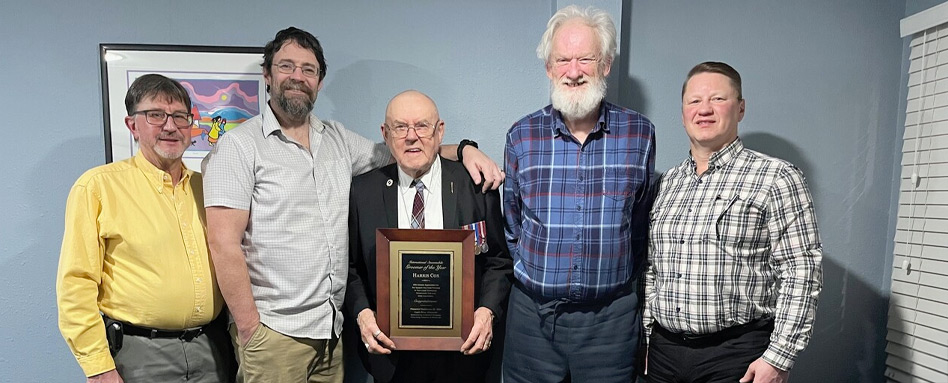 5 men standing and smiling in a room with a man holding a plaque