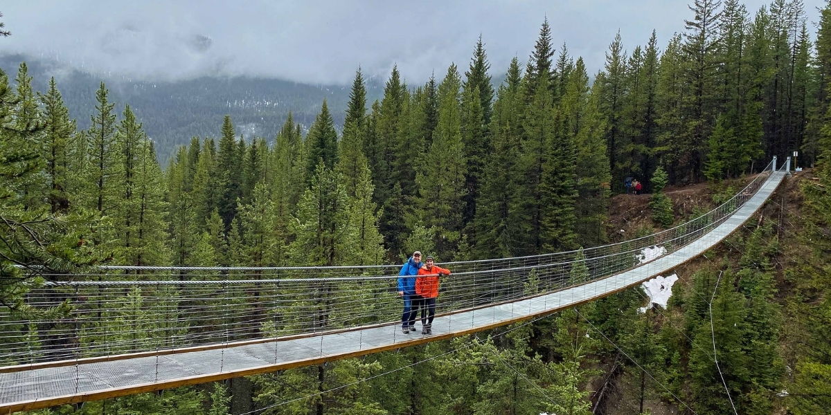 two people on a bridge overlooking large forest and sea