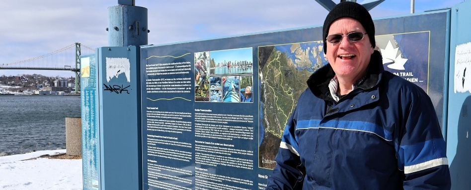 01Support image_HRM web story_David Rodenhiser-Dartmouth Harbourfront Trail_credit Cathy Donaldson | Sentier Transcanadien man standing in front of trail signage smiling on a sunny and snowy day