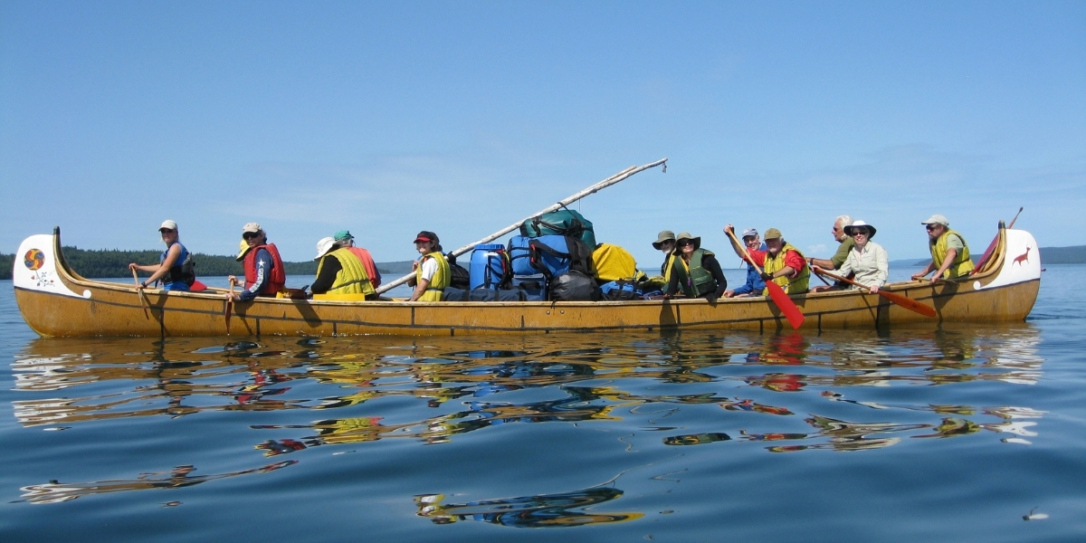 00Feature image_Naturally Superior story_credit Naturally Superior | Sentier Transcanadien people in a large canoe paddling on a lake on a sunny day