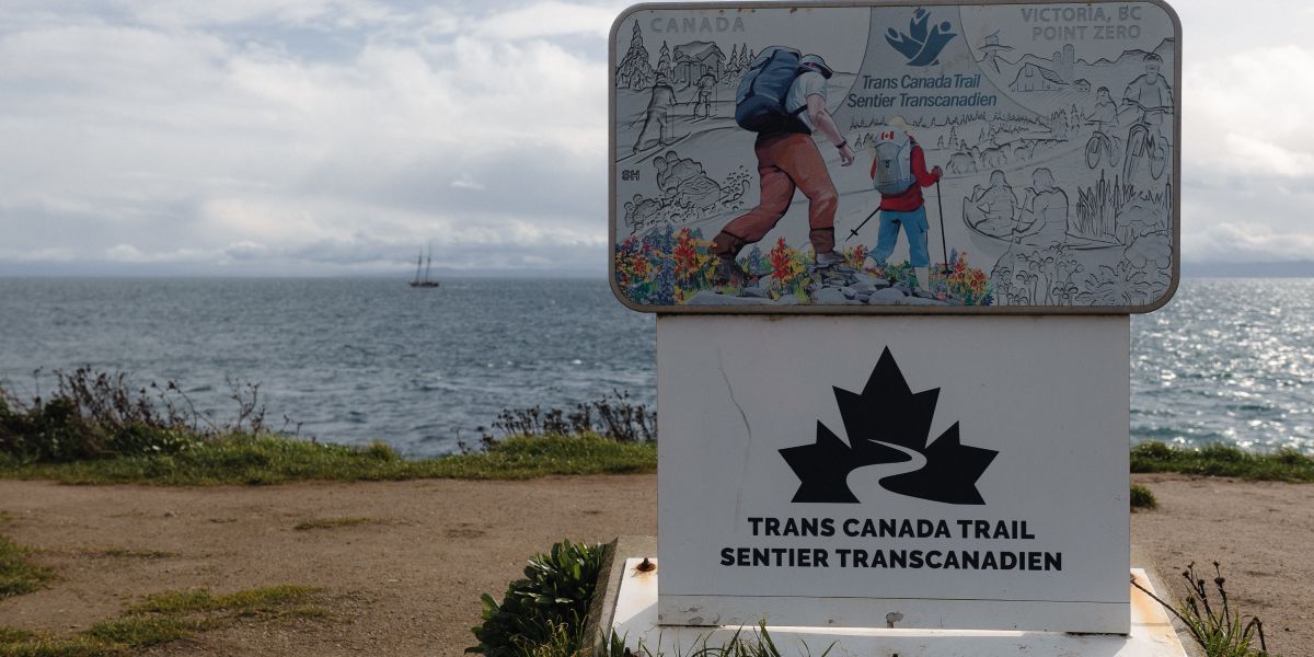 00Feature image_Victoria - Dallas Road - 10_credit Meg Pender | Sentier Transcanadien signage on a trail of man and boy hiking with water behind