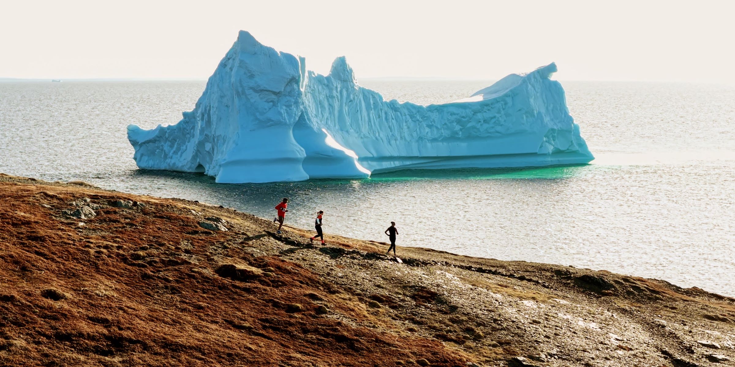 Trail Run Photo-GNT-webcrop | Sentier Transcanadien People run on the Atlantic coast along the Great Northern Trail with an iceberg in the background.