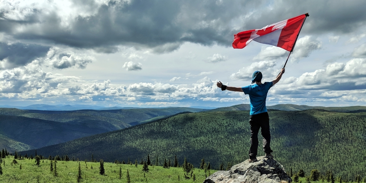 man holding a canadian flag on a mountain top on a cloudy day