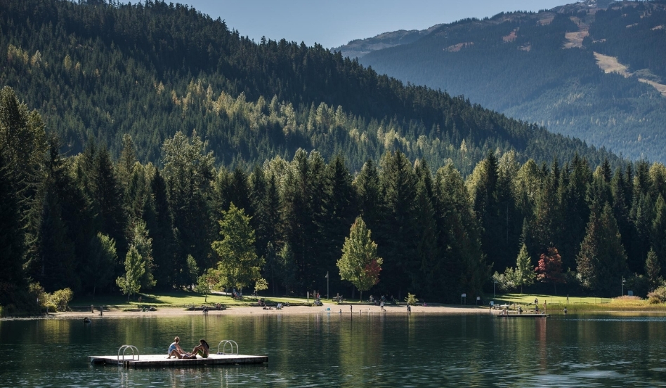 02Support image_Whistler Museum story_Lost Lake_credit Destination BC-Blake Jorgenson | Sentier Transcanadien large dock with two people sitting overlooking a lake and rolling mountains