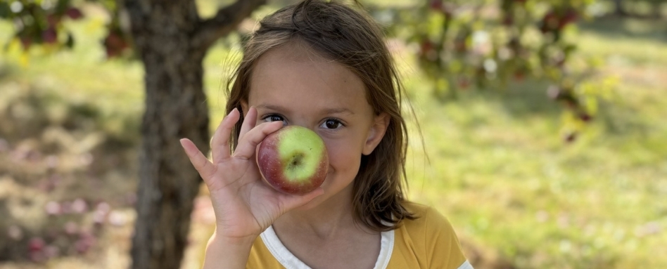 03Support image_Veloroute gourmande_credit Amy Schwartz | Sentier Transcanadien child smiling and holding an apple up to her face