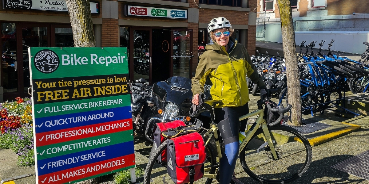 00Feature image_Leigh McAdam bikepacking_credit Leigh McAdam | Sentier Transcanadien woman in front of signage posing with bikes