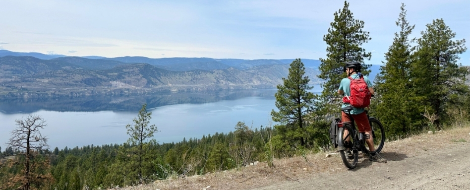 person cycling on dirt trail overlooking sea and forest